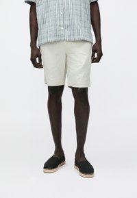 Lichtgekleurde linnen shorts hebben een losse pasvorm en worden gecombineerd met een contrasterend, gestructureerd grijs-blauw gestreept overhemd en zwarte espadrilles met gevlochten zolen.