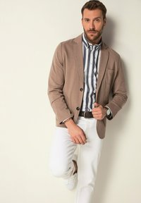 Blazer marrone chiaro su una camicia a righe blu e bianche, abbinata a pantaloni bianchi e sneakers bianche. Dettagli notevoli includono una tasca e polsini con bottoni.
