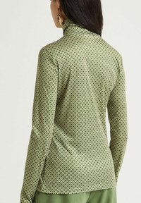 Top verde a maniche lunghe con un colletto alto caratterizzato da un motivo geometrico in verde scuro e nero. Tessuto morbido e strutturato.