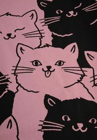 Różowy materiał z ilustracjami czarnych kotów, z wyraźnymi wyrazami twarzy i konturami, tworzący wesoły wzór na powierzchni.