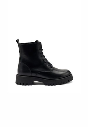 Botte de combat en cuir noir à lacets, avec semelle épaisse à crampons et languette à l'arrière, vue du côté extérieur sur fond blanc.