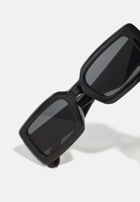 Lunettes de soleil noires avec une finition brillante. Verres sombres, montures épaisses et bords arrondis. Pas de marque visible ni de détails supplémentaires.