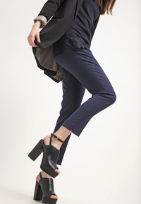 Marina smal passform byxor med en jämn yta, kombinerat med svarta öppna klackskor med tjock klack och rem runt vristen.