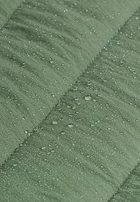 Gros plan d’un tissu vert déperlant avec des gouttes d'eau visibles perlant à la surface, montrant sa qualité imperméable.