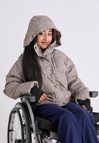 Light grey puffer jacket with a hood, featuring elastic cuffs. Worn over navy pants, the individual is seated in a wheelchair.