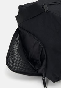 Geantă neagră cu un exterior texturat și un compartiment cu fermoar. Prezintă un detaliu din plasă pe o latură și o căptușeală din material neted în interior.