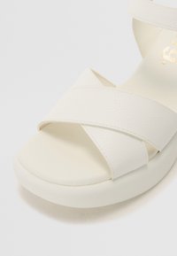 Sandal en synthétique blanc avec des brides croisées et un bout arrondi. Texture lisse avec une semelle rembourrée pour le confort.