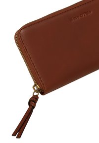 Braune Lederbörse mit einem Reißverschluss, goldfarbenem Zipper und einem Lederquasten. Mit geprägtem "Marc O'Polo"-Logo. Glatte Textur.