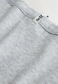Tissu à côtes gris avec une surface texturée. Présente une étiquette labellisée "self" cousue sur le bord supérieur. Lisse et légèrement extensible.