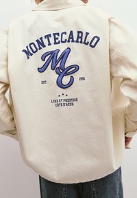Beige jacket featuring a large navy embroidered "MONTECARLO" and "MC" on the back, with additional text and stars below.