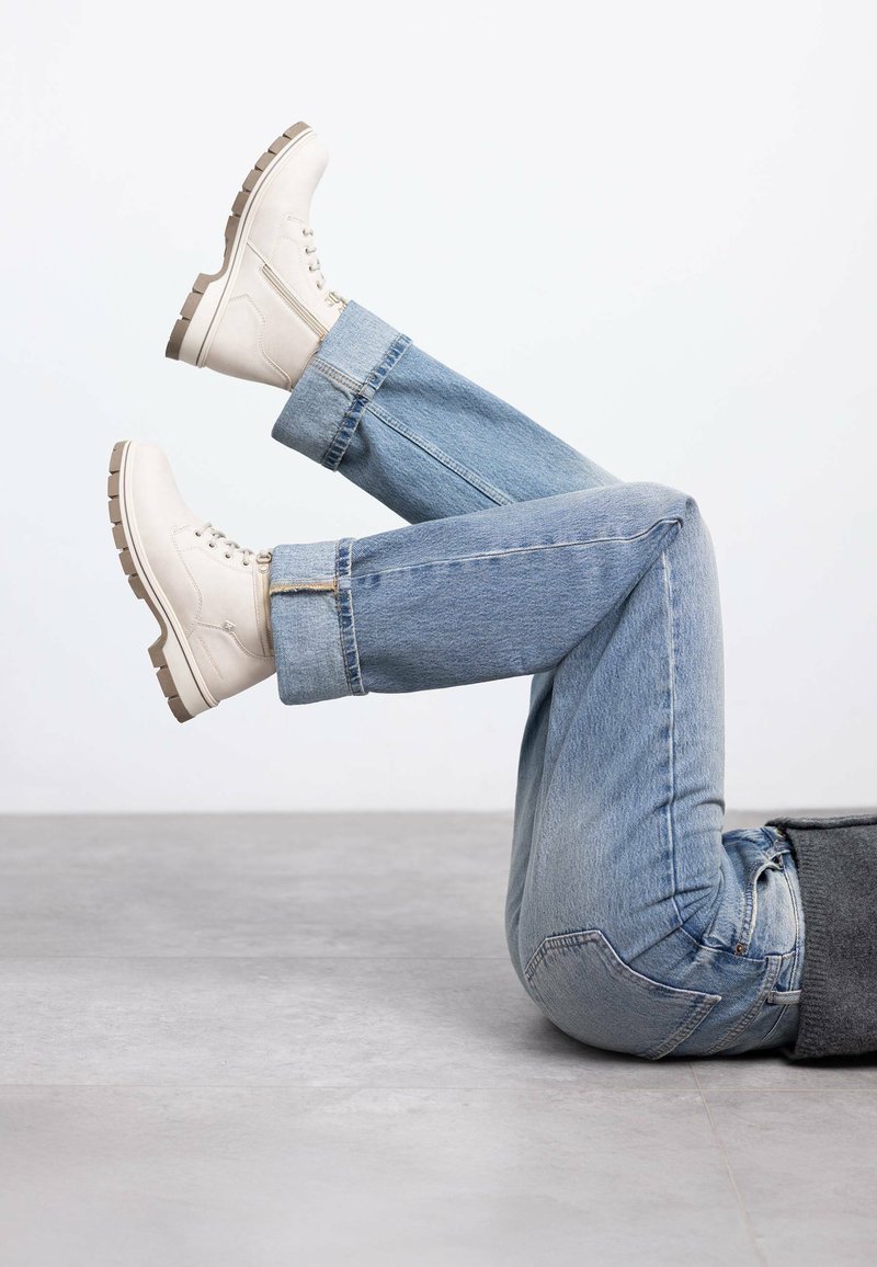 Botas de tobillo blancas con punteras redondeadas y suelas gruesas, combinadas con jeans de mezclilla azul claros, que muestran un ajuste relajado y casual.