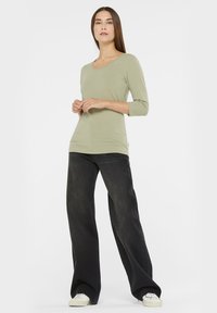 Light green long-sleeve top with a scoop neckline, paired with loose, dark denim jeans and white sneakers. Smooth fabric, casual fit.