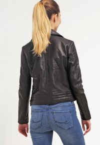 Black leather jacket with a fitted design, smooth texture, and structured shoulders. Finished with horizontal seams at the waist.