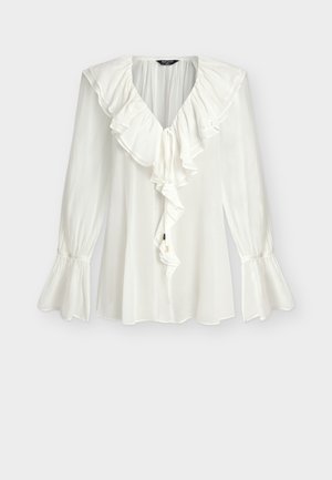 Λευκό μπλουζάκι με μακριά μανίκια, V-λαιμόκοψη με βολάν, καταρράκτη βολάν μπροστά και φουσκωτά, σούρες στις μανσέτες.