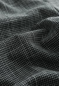 Czarnobiały materiał w strefy houndstooth, charakteryzujący się teksturowanym splotem z subtelnym połyskiem, ukazującym skomplikowane detale wzoru w całej tkaninie.