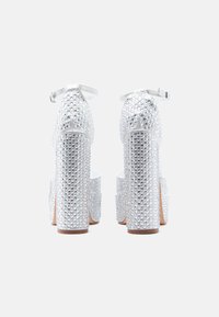 Stříbrné sandály na vysokém podpatku se strukturovaným povrchem zdobeným kamínky a masivním platformovým podpatkem. Nastavitelný pás kolem kotníku.