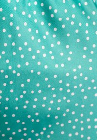 Una tela de color azul verdoso con una textura suave presenta puntos blancos distribuidos uniformemente por toda la superficie, creando un patrón juguetón.