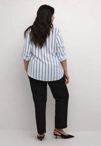Chemise bleu clair à manches longues avec des rayures verticales noires, assortie à un pantalon noir et des mocassins à talons noirs. Texture de tissu lisse.