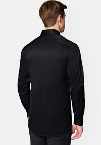 Czarna koszula z długim rękawem o gładkiej, błyszczącej fakturze, standardowym kołnierzyku i zapinanych mankietach. Widoczne szwy oraz wygięty krój dołu.