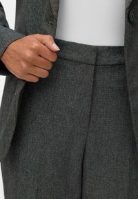 Mørkegrå dress med teksturert stoff og subtile mønstre, kombinert med en matchende blazer og en tettsittende hvit topp under.