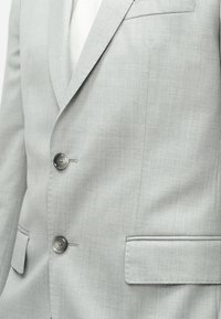 Γκρι σακάκι με λείο υφή, δύο κουμπιά, μια τσέπη στο στήθος και δύο μπροστινές τσέπες. Διαθέτει σχέδιο με εγκοπή στα πέτα.