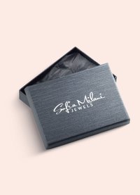 Sort tekstureret smykkeboks med hængslet låg, der har "Sofia Milani Jewels" logoet i hvidt. Indeholder sort indreforing.