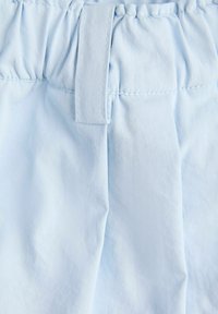 Pantalon bleu clair à taille élastique avec passant de ceinture et coutures visibles sur le tissu.