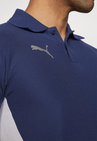 Námořnická polo košile vyrobená z texturované látky, s jemným šedým logem Puma na hrudi a bílým panelem na boku.