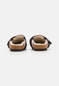 Brune bakløse sko med teksturerte korksåler og myk kremfarge innersåle. Har minimalistisk design med dekorative detaljer på stroppene.