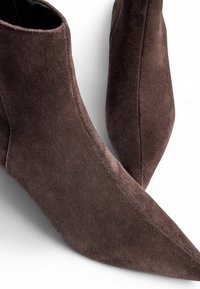 Bottines en suède marron avec un bout pointu et une texture lisse, au design élégant et minimaliste, dotées d'une fermeture éclair sur le côté.