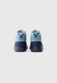 Une paire de bottes d'hiver en suède bleu clair avec des semelles en caoutchouc noir, vues de l'arrière sur fond blanc.