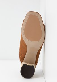 Chaussure en daim marron avec une semelle en cuir lisse, présentant des détails cousus et un accent de talon tissé. Étiquette de taille visible indiquant "37".