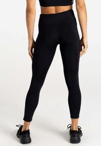 Schwarze, hochtaillierte Leggings aus dehnbarem Stoff, mit glatter Textur und taillierter Passform. Ergänzt durch schwarze Sportschuhe.