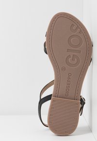 Semelle de sandale avec le logo Gioseppo, taille 35, montrant la bande de roulement texturée et des sangles noires avec boucle sur fond blanc.