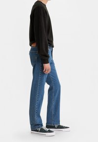 Sudadera negra, vaqueros azules de pierna recta y zapatillas negras con suelas blancas. Detalles notables incluyen puños acanalados y textura de denim.