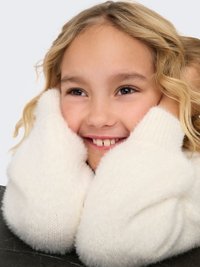 Weißer, flauschiger Pullover mit weicher Textur, umrahmt ein Gesicht mit hellbraunem, welligem Haar und einem Lächeln, das kaum Zähne zeigt.