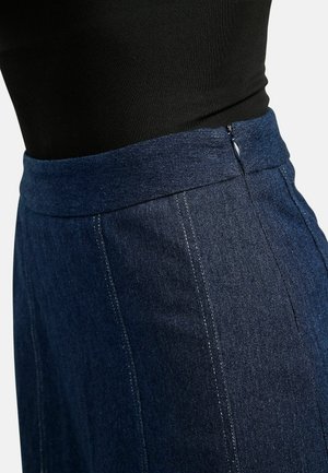 Tamsiai mėlynas džinsinis sijonas su lygiu paviršiumi, išsiuvinėtas baltomis siūlėmis, aukštu liemeniu ir užtrauktuku gale.