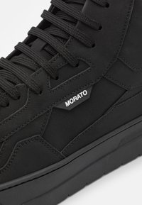 Czarny wysoki sneaker z grubymi sznurowadłami, szczegółowym przeszyciem oraz metką z logo "MORATO" po bokach ponad grubą podeszwą.