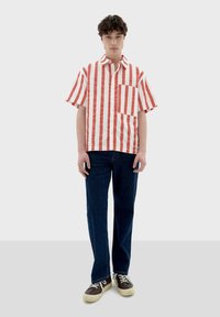 Kortärmad röd och vit randig skjorta med krage och bröstficka, kombinerad med mörkblå jeans och avslappnade sneakers.