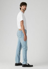Jeans de mezclilla azul claro con corte recto, combinados con una camiseta blanca sencilla y mocasines negros. Presentan costuras traseras y un parche de cuero.