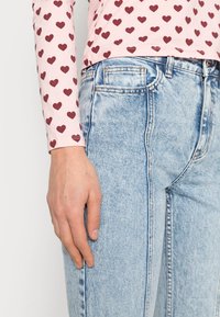 Camisola de mangas longas rosa claro com padrões de corações cor de vinho, combinada com jeans de ganga de cintura alta azul claro com um design clássico de cinco bolsos.