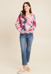 Pull multicolore avec des motifs roses, bleus et navy, d'une texture douce ; associé à un jean bleu clair et des baskets roses brillantes.