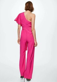 Combinaison fuchsia à une épaule avec une manche volantée, présentant une taille cintrée et un design à jambes larges, fabriquée à partir d'un tissu lisse et texturé.