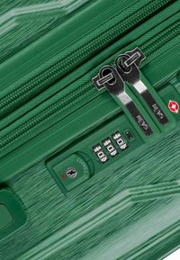 Groene harde koffer met een textuurafwerking, dubbele metalen ritsen, combinatie slot en een sleuf voor een sleutel aan de zijkant.