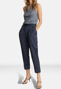 Pantalon en velours marine avec une coupe décontractée et des plis, associé à un haut sans manches gris clair avec un panneau texturé et brillant.