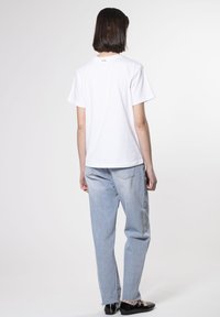 Camiseta de algodón blanca con un corte relajado, con mangas cortas y un pequeño logo en la parte posterior. Combinada con jeans de pierna recta en un tono azul claro.