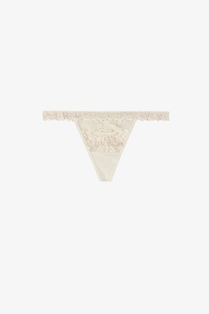 String beige en dentelle avec panneau avant en dentelle florale et ceinture en dentelle festonnée sur fond blanc.