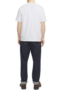 Camiseta blanca de manga corta con cuello redondo, combinada con jeans azul oscuro, con los puños remangados, y calzado marrón.