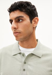 Lichtgroene polo met een textuurstof. Heeft een klassieke kraag en een drie knoopjessluiting. Draag het over een wit t-shirt met ronde hals.