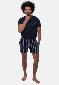 T-shirt blu navy con taschino sul petto abbinato a pantaloni corti a righe blu e bianche. I pantaloni corti hanno una vita elasticizzata e sono lunghi fino al ginocchio.